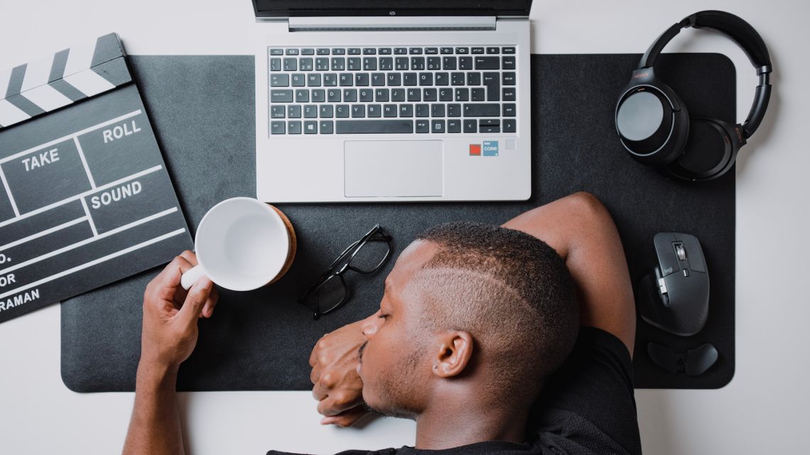 man sleeping at a desk while holding a cup