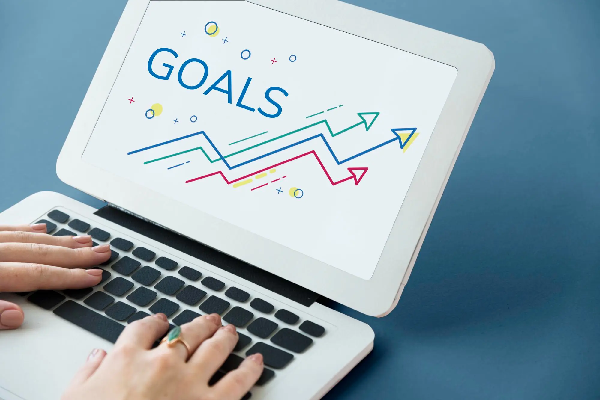 Hands typing on a laptop showing the word Goals above rising arrows